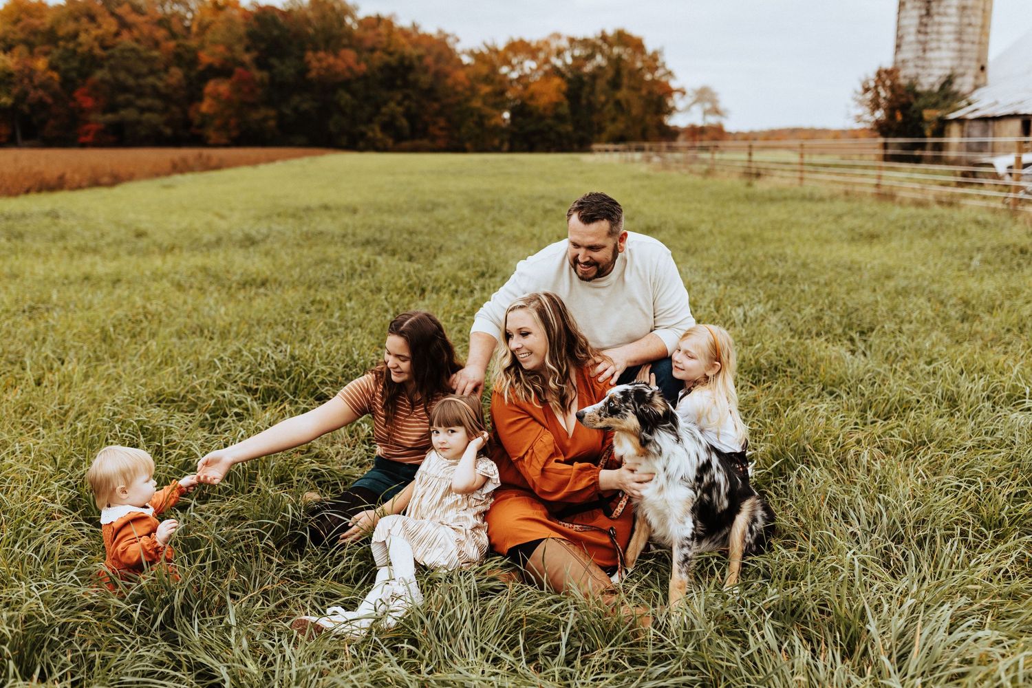 Happy family with three children and an Australian Shepherd dog sitting in a lush green field in autumn.