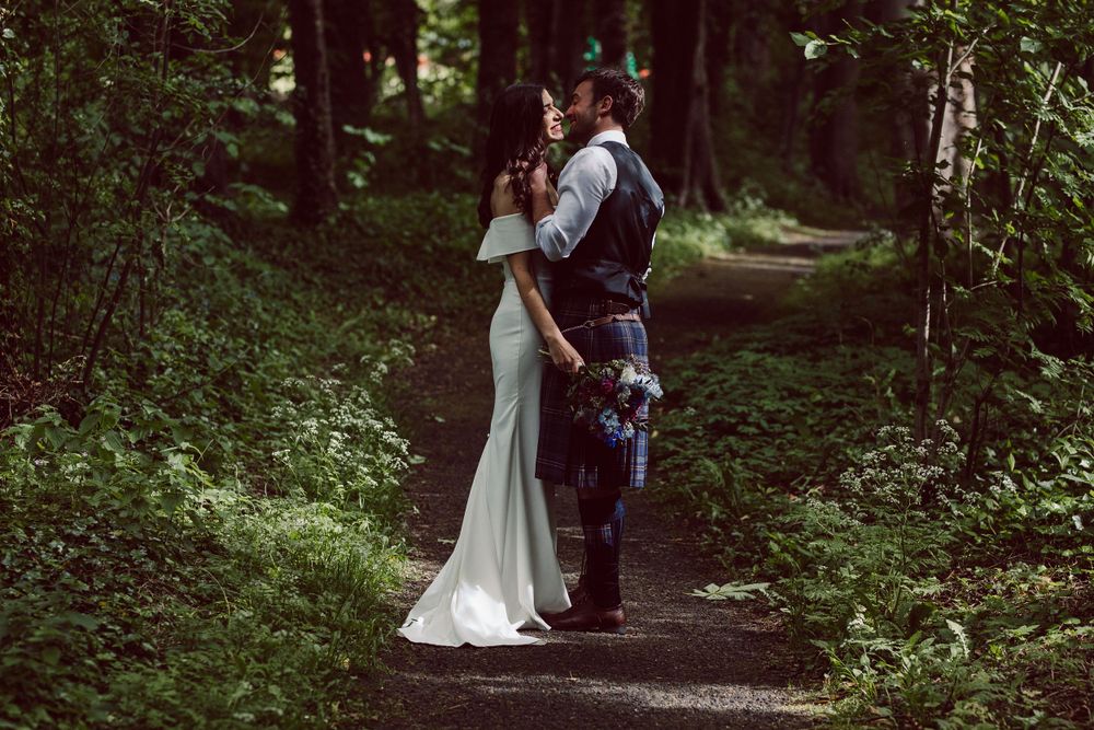 Bride and Groom embrace on a path in the woods in sunlight