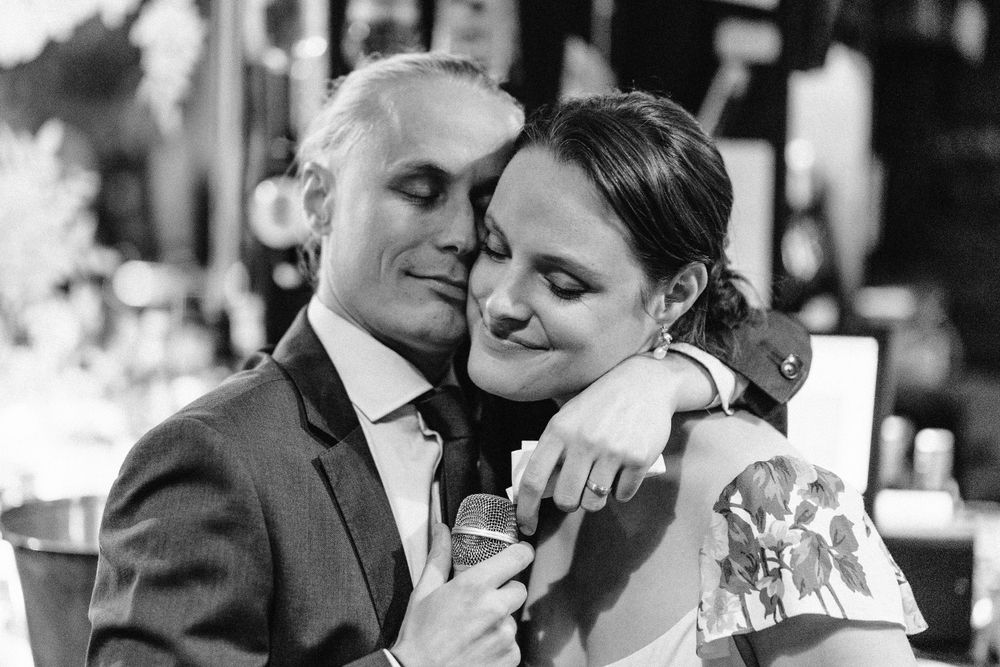 groom hugs bride with cheeks touching and drink in his hand