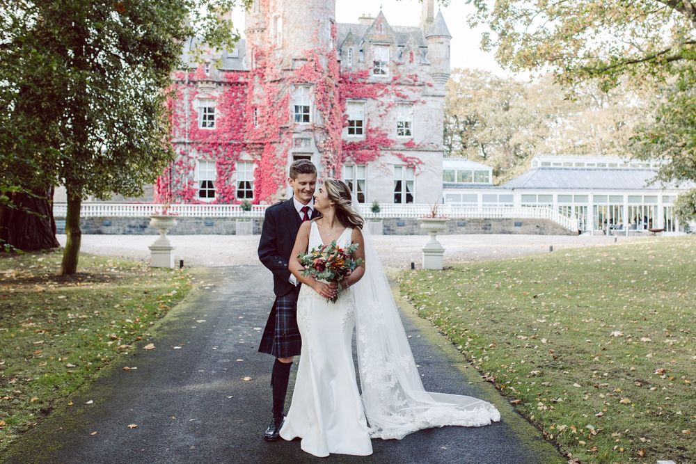 Bride and groom hug in front of Scottish castle that is covered in red ivy