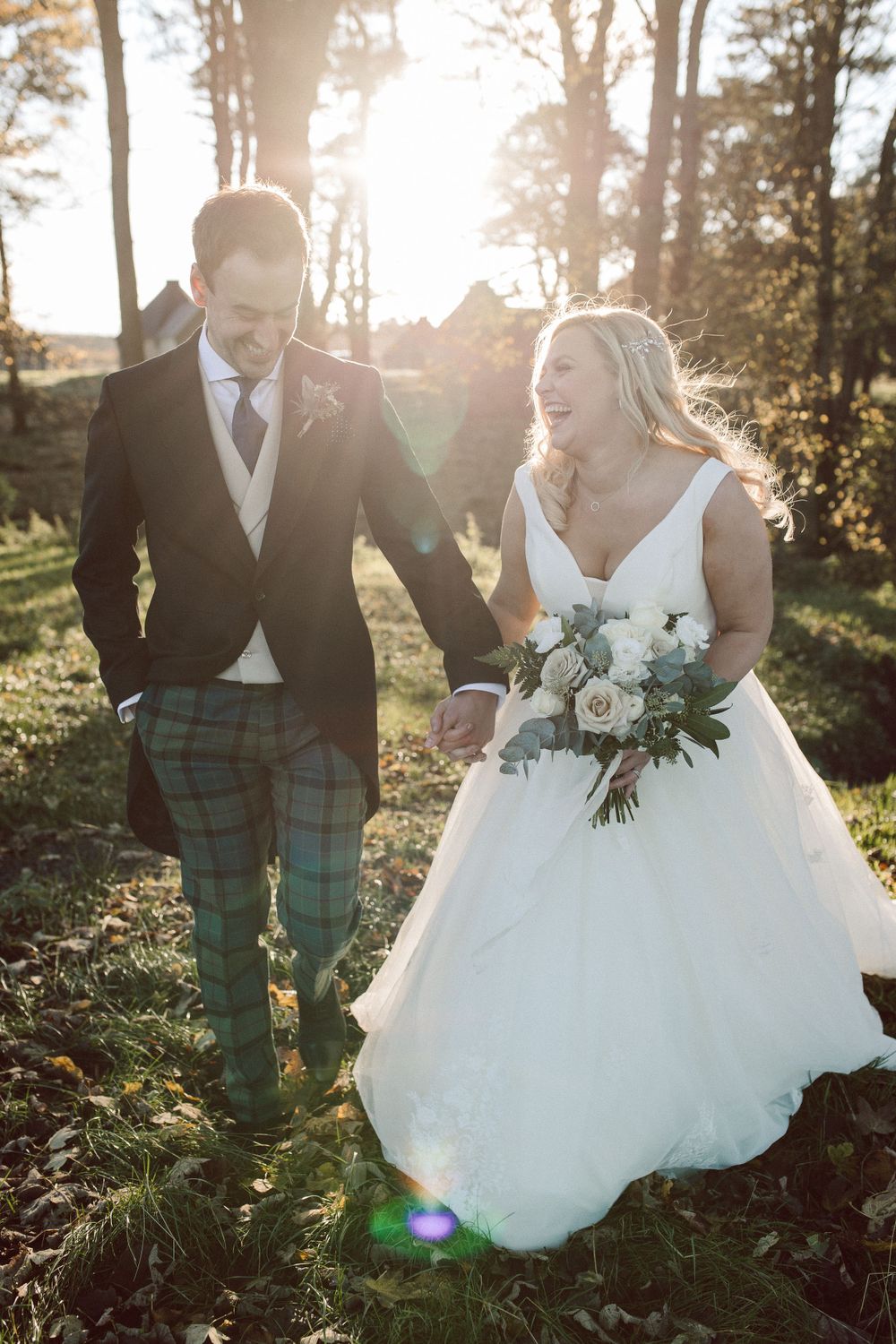 Bride and groom walk through the woods with golden sunlight
