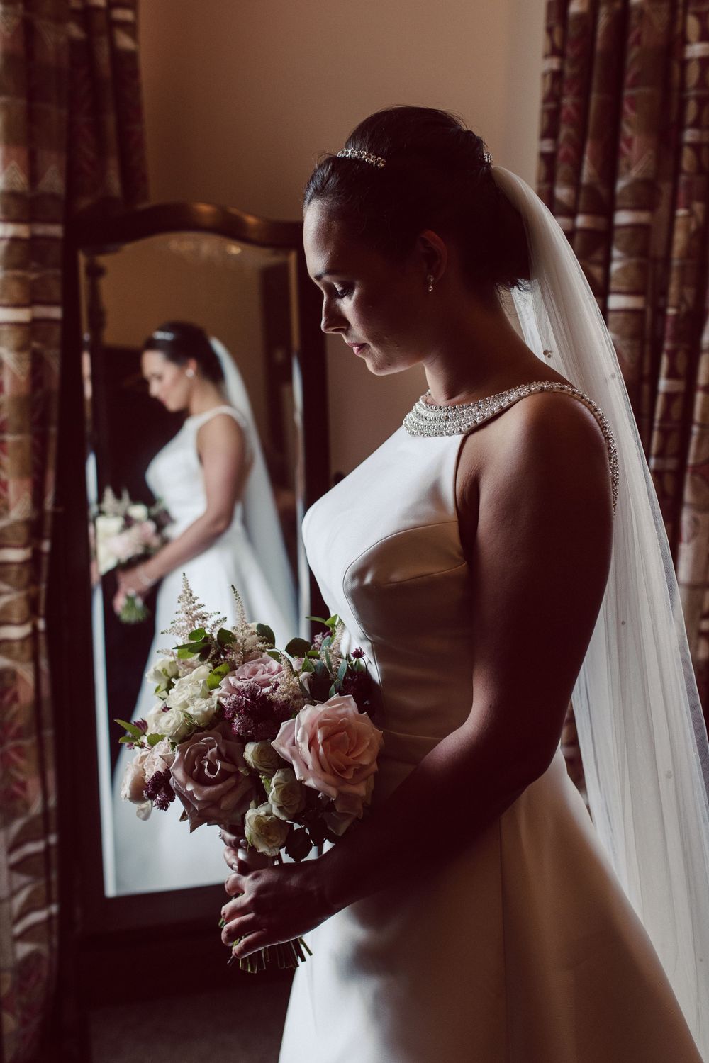 beautiful bride looking down at her bouquet in front of a mirror