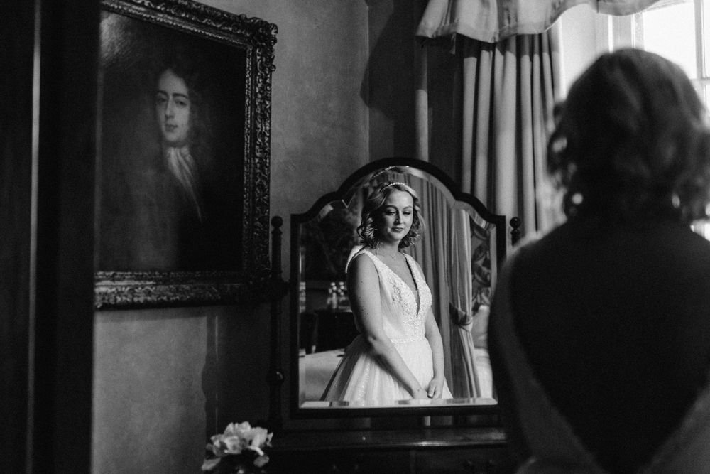 bride looking out of the window with a reflection of her in a mirror
