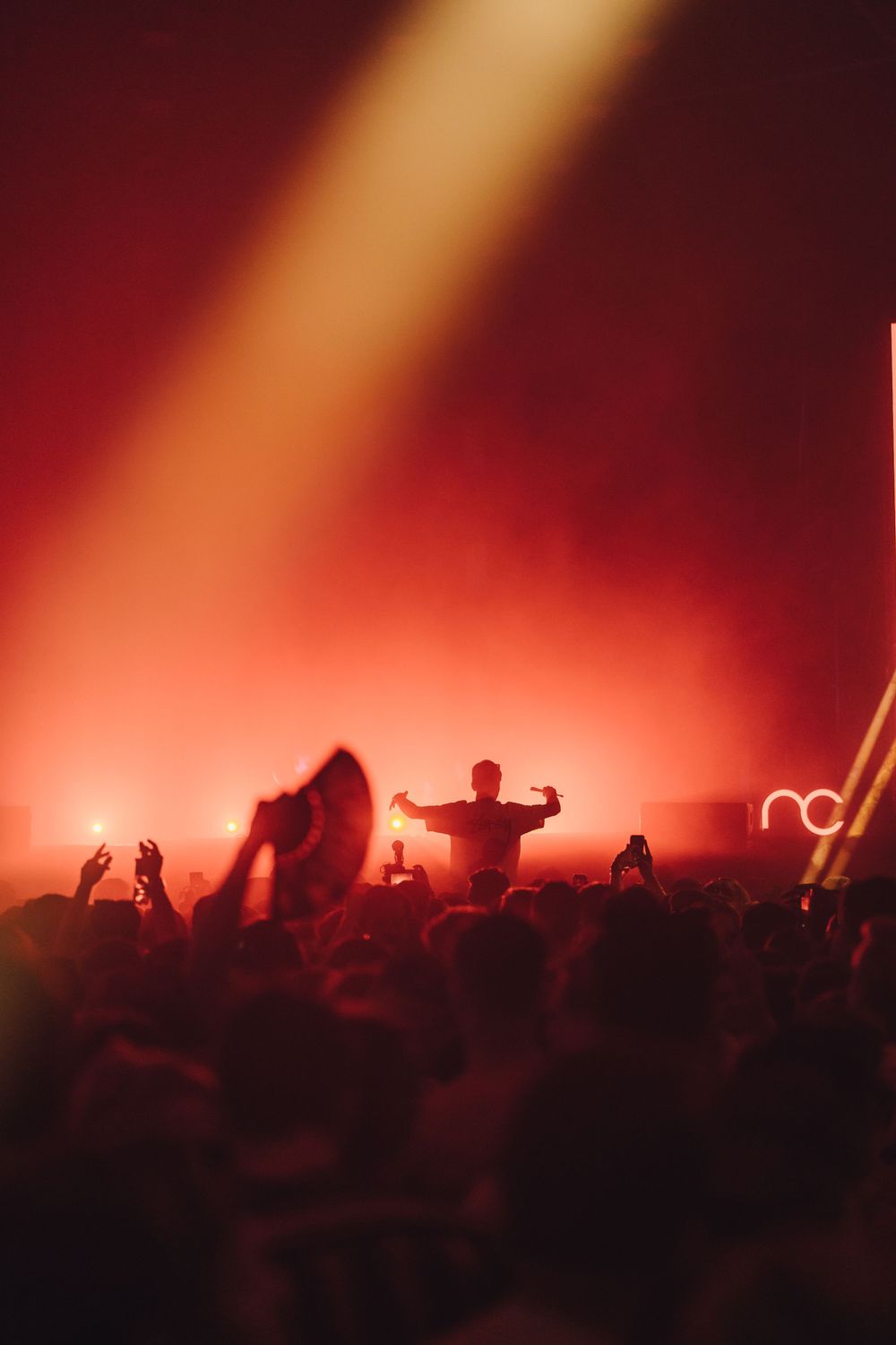 Silhouetted crowd at a concert with dramatic orange lighting and smoke effects.