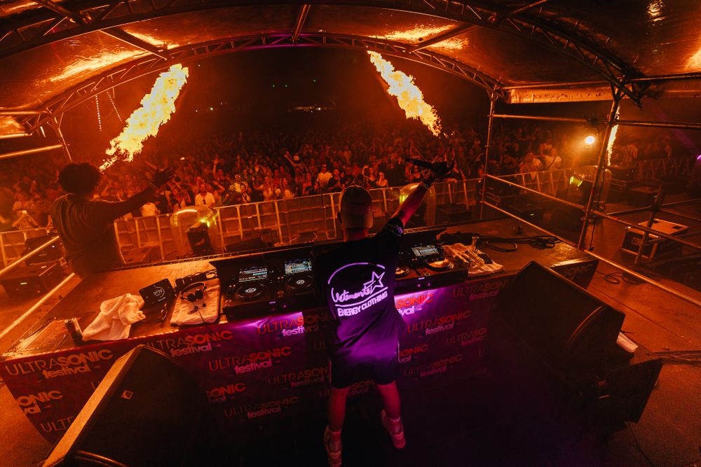 Concert venue with dramatic flame effects and DJ booth illuminated in orange light.