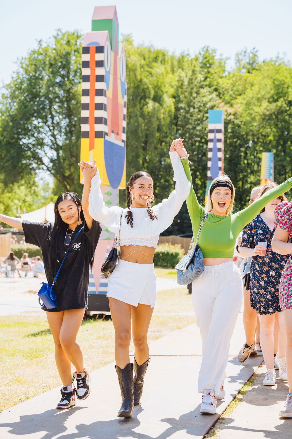 Three friends in colorful outfits jumping and celebrating at a summer festival.