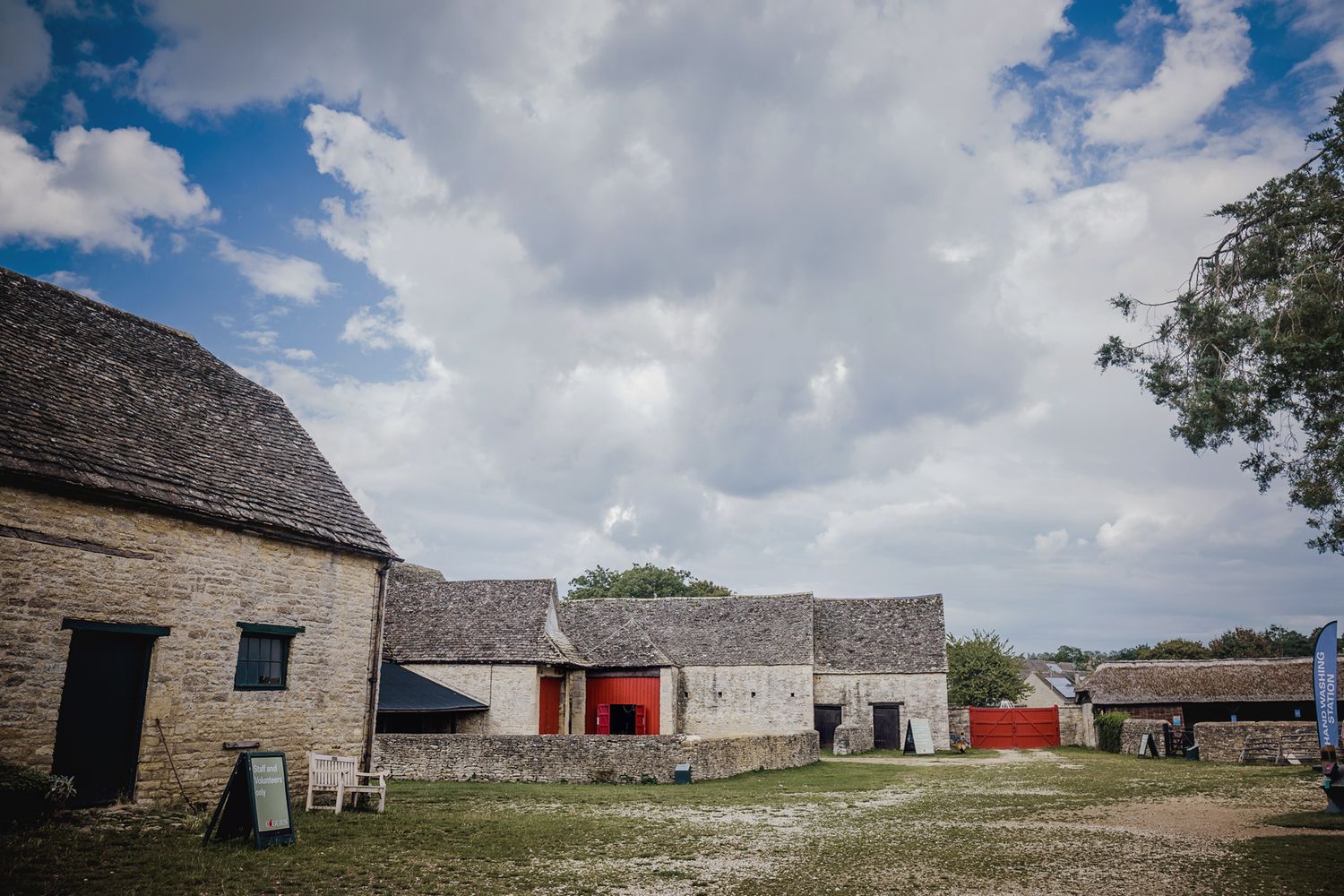 Historic stone farm buildings with thatched roofs under cloudy sky in rural setting.