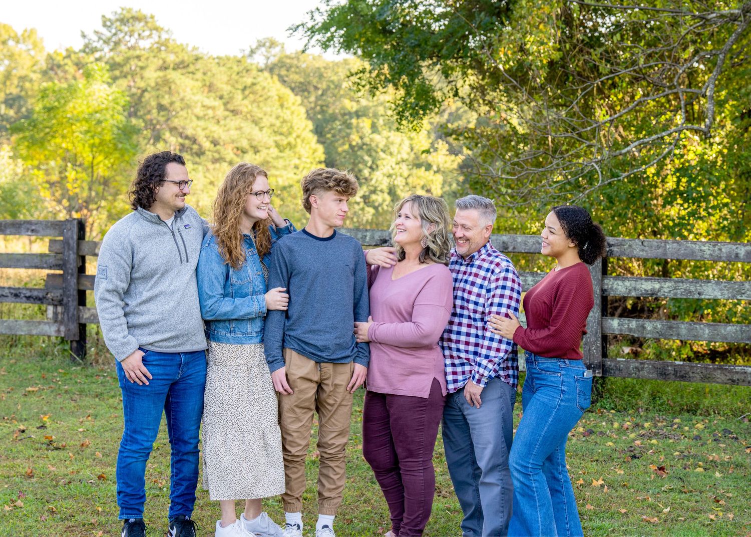 Group of friends laughing together outdoors by a wooden fence during golden hour.