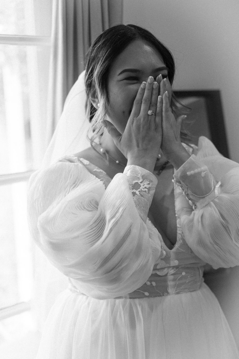 A glimpse of an emotional moment in a wedding dress with billowing sheer sleeves against natural window light.