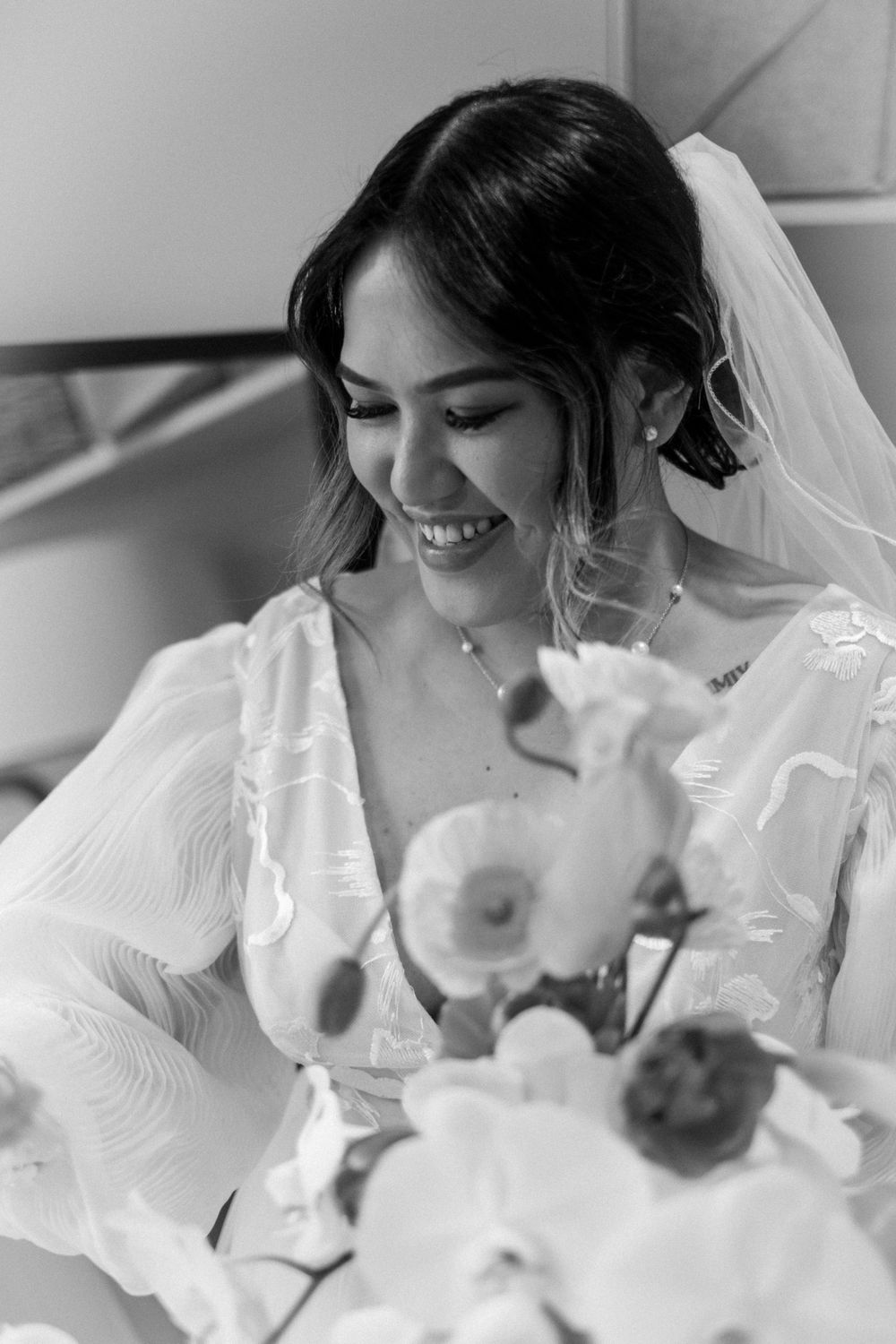 A black and white portrait of a bride smiling with orchids in the foreground.