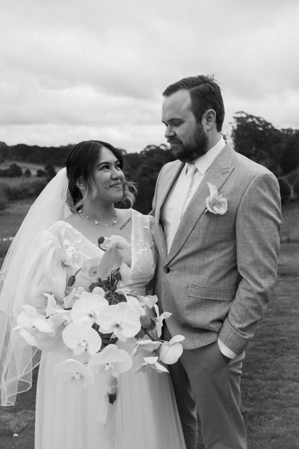 Romantic outdoor wedding portrait with a bouquet of white flowers against a countryside backdrop.