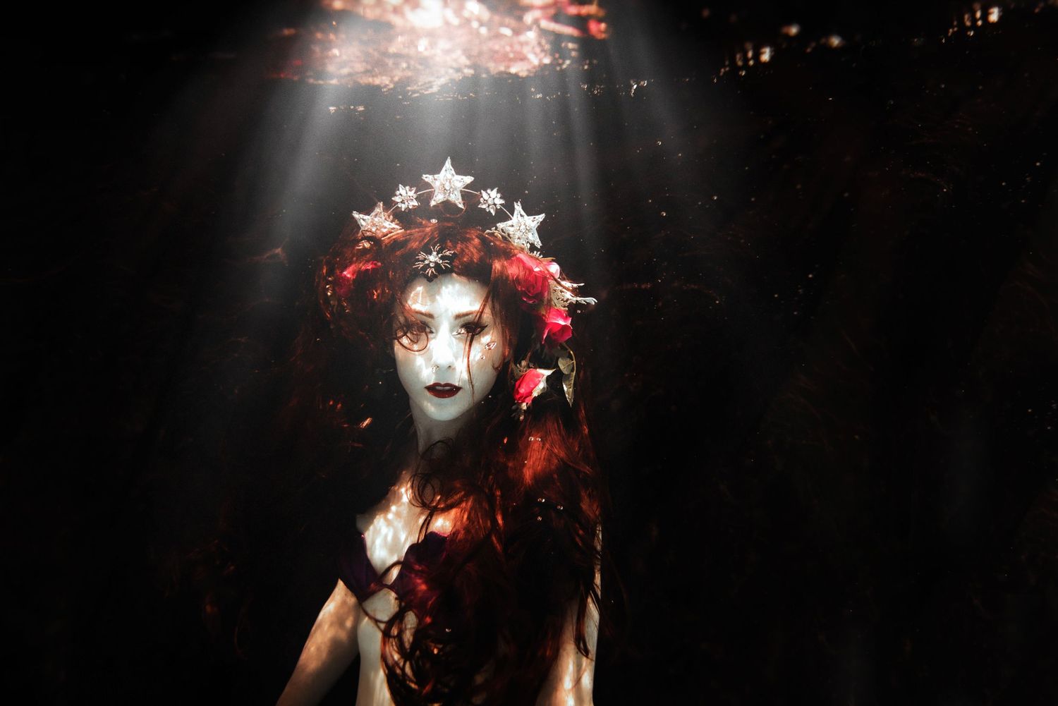 Dark underwater portrait with crowned figure and dramatic light beams.