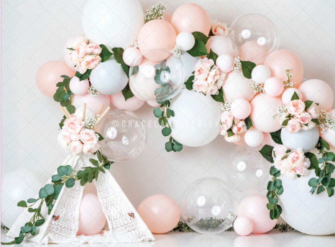 Elegant balloon arch installation with blush pink, white and clear balloons adorned with eucalyptus greenery against white wall.