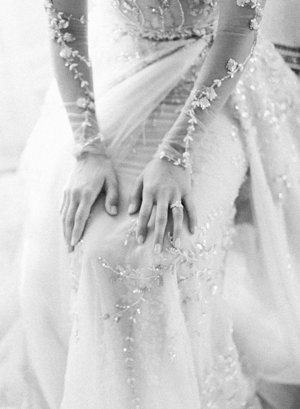 Close-up detail of delicate lace embellishments and wedding ring on a white wedding dress.
