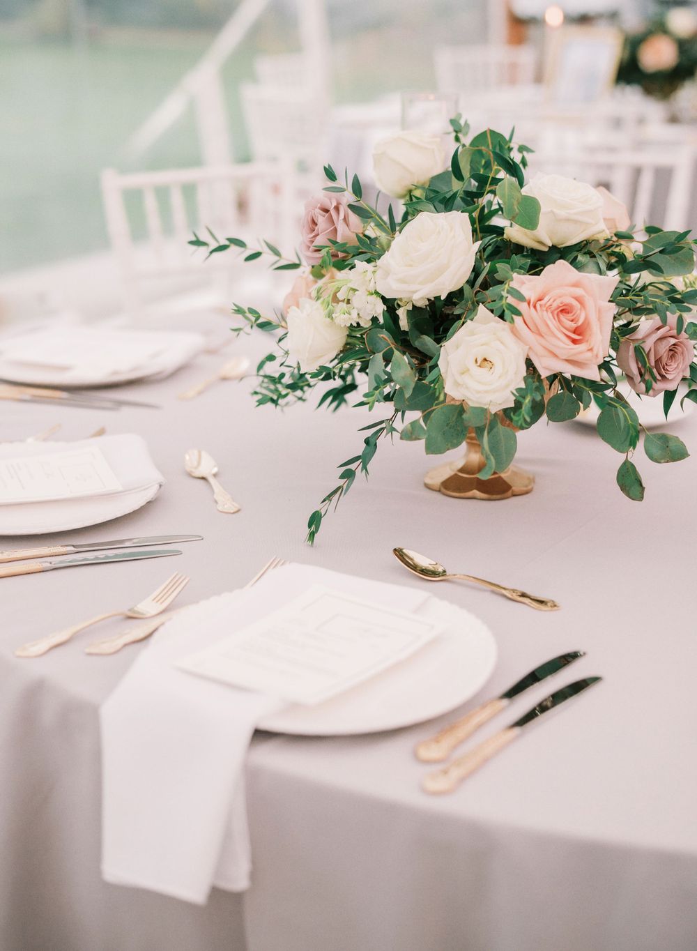 Elegant table setting with pink and white rose centerpiece and gold flatware for a wedding reception.
