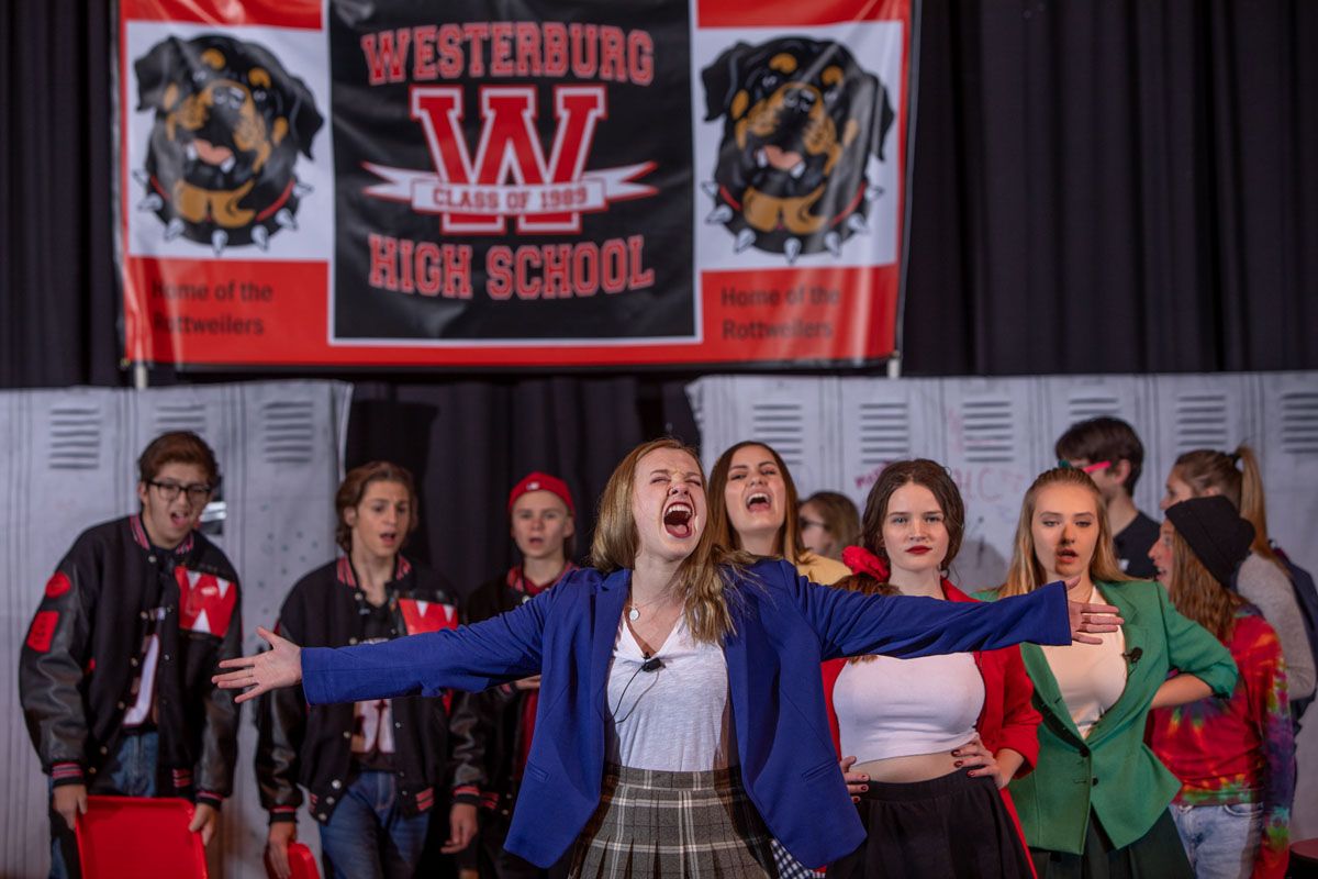 Students perform in front of school lockers with a Westerburg High School banner displayed in the background.