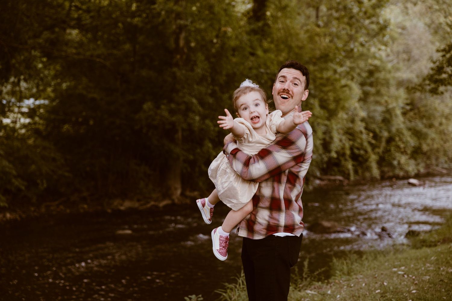 A joyful outdoor moment captured by a river showing playful interactions in a plaid shirt.