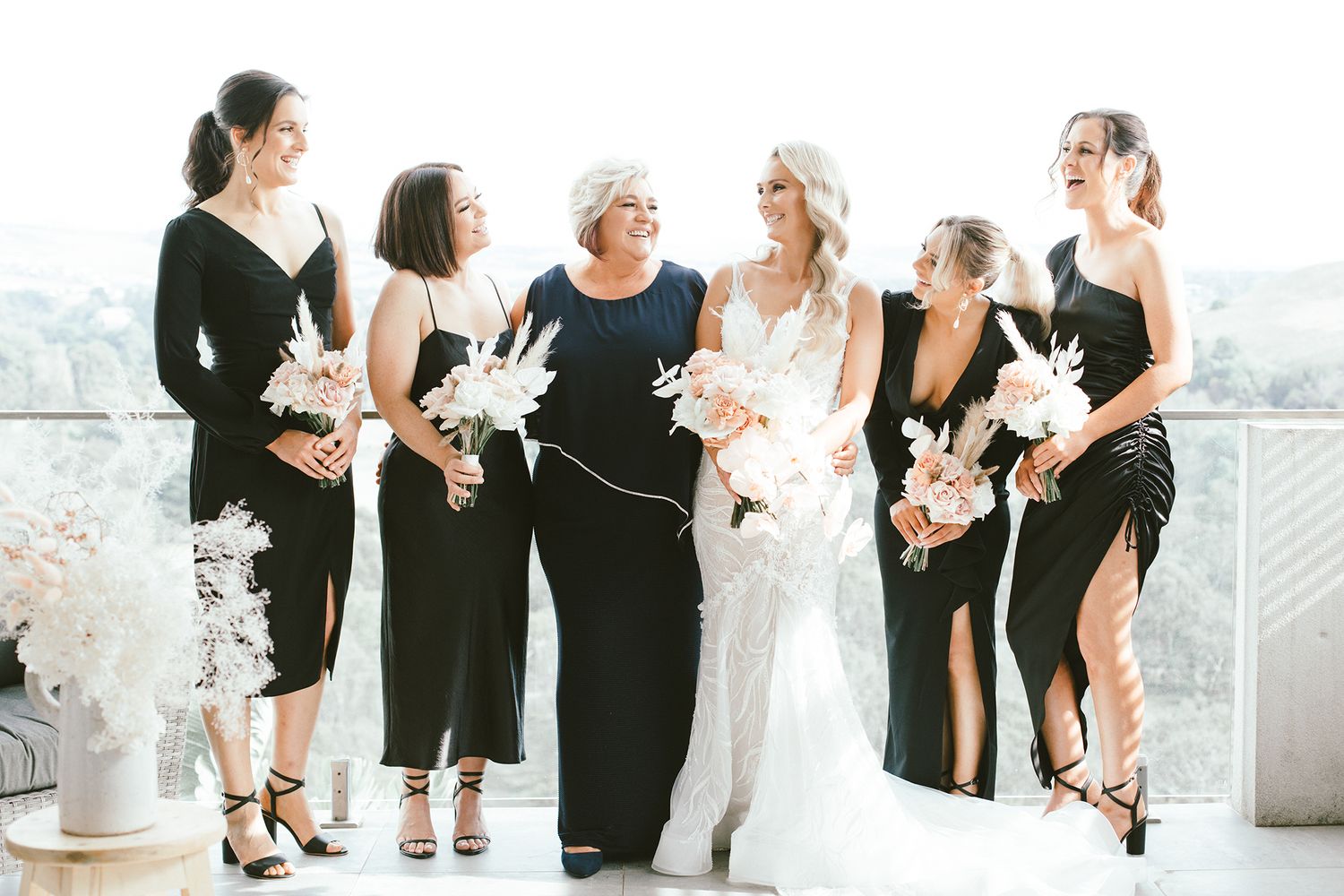 Wedding party sharing joyful moment together in black dresses with white floral bouquets.