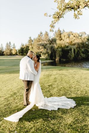 A couple shares an intimate moment on their wedding day in a sunlit garden with trailing bridal veil.