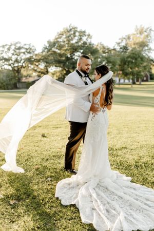 Newlyweds embrace on a lawn as the bride's lace gown and veil catch the golden sunlight.