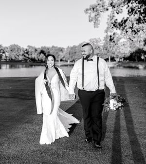 A black and white portrait of newlyweds walking together across a garden lawn.