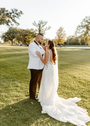 Newlyweds share a tender moment on a sunlit lawn with her lace gown flowing beautifully.