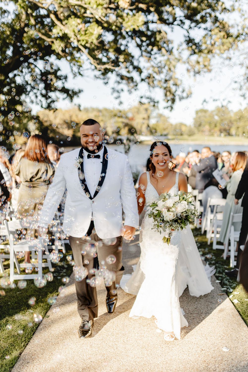 Happy newlyweds exit their outdoor ceremony along a path lined with wedding guests.