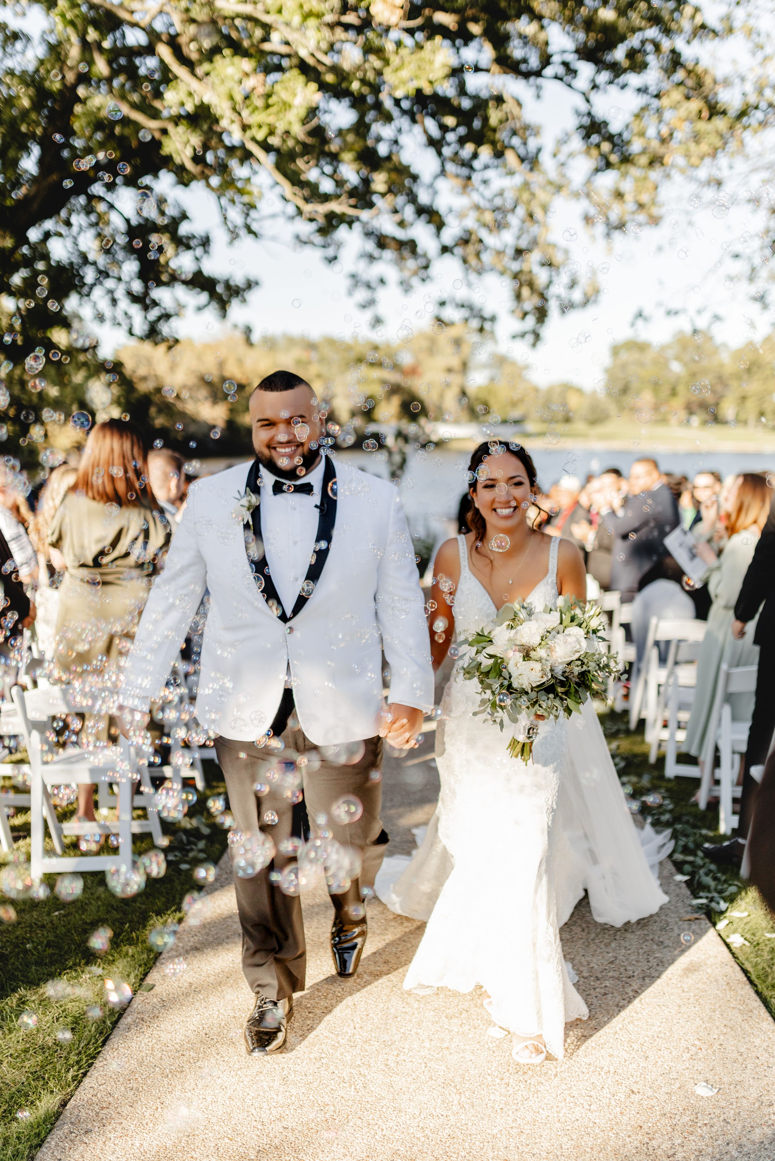 Happy newlyweds exit their outdoor ceremony along a path lined with wedding guests.