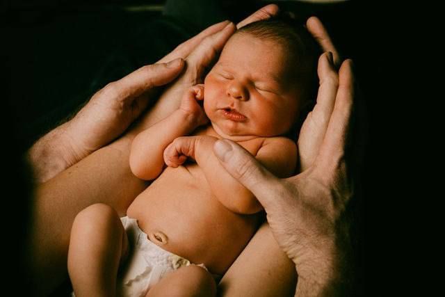 A peaceful sleeping newborn nestled in caring hands against a dark background.