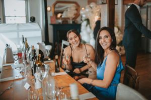 Wedding reception guests enjoying conversation at tables by waterfront windows.