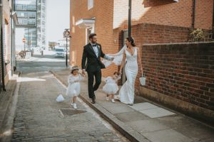 Couple walks along a brick pathway outside while guests prepare to celebrate.