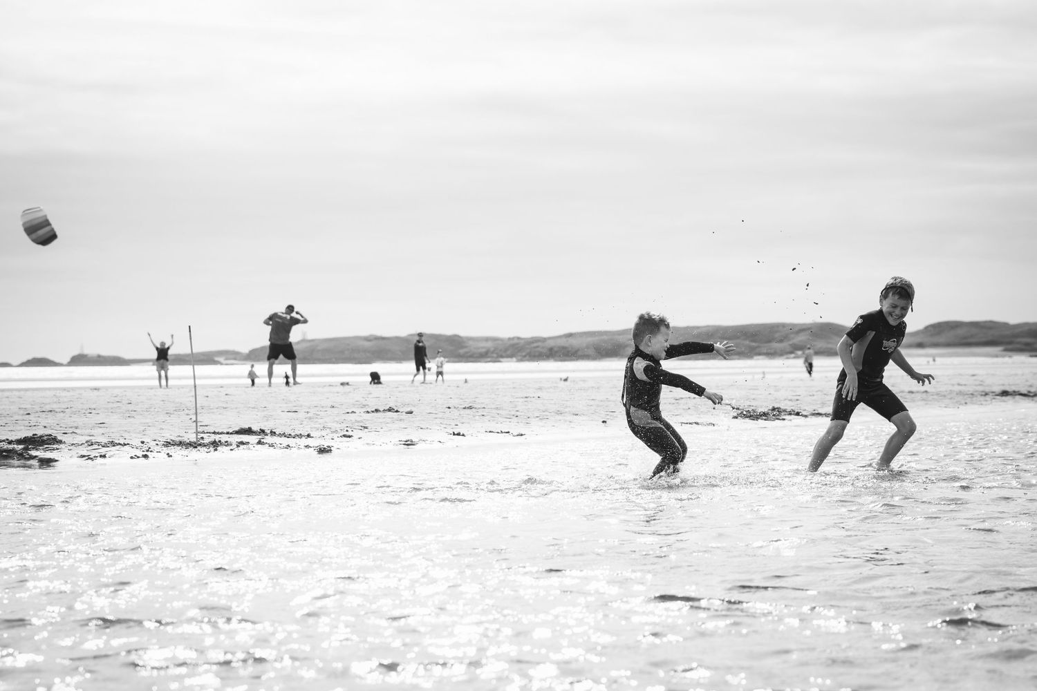 Black and white beach scene with people playing and running on the sand.
