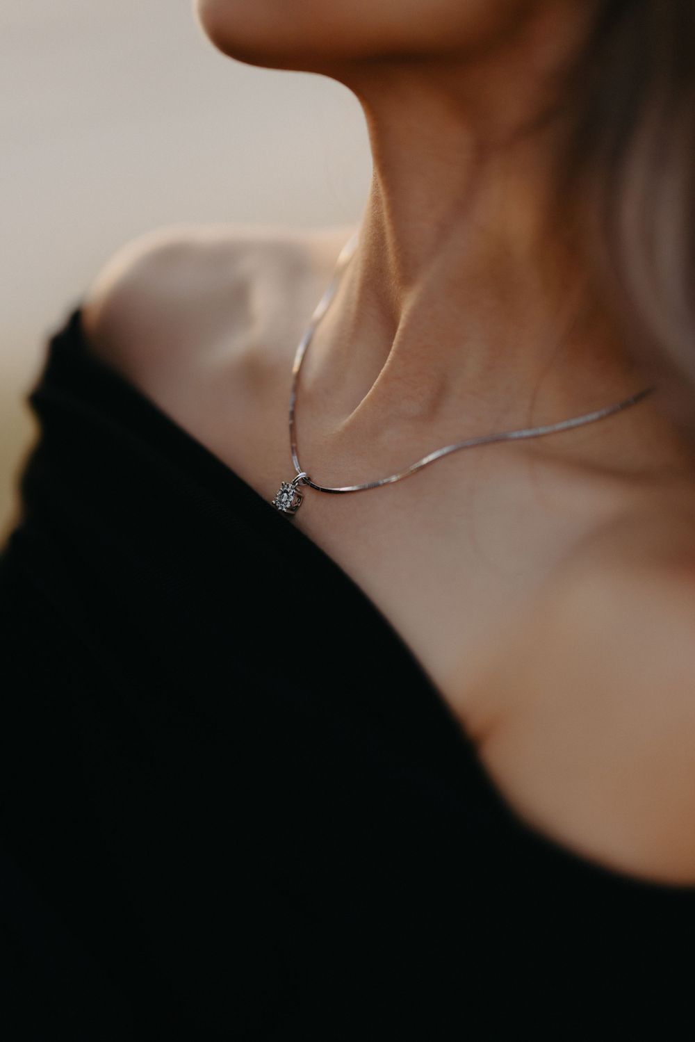 Close-up of a delicate silver necklace with pendant worn against a black top.