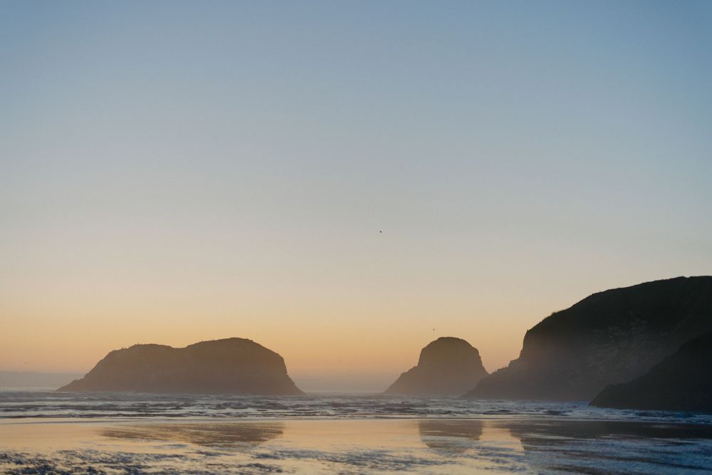 Dramatic coastal landscape with rocky sea stacks silhouetted against a golden sunset.