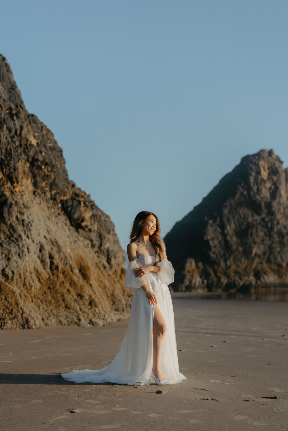 Ethereal bridal portrait on beach with dramatic coastal cliffs in background.