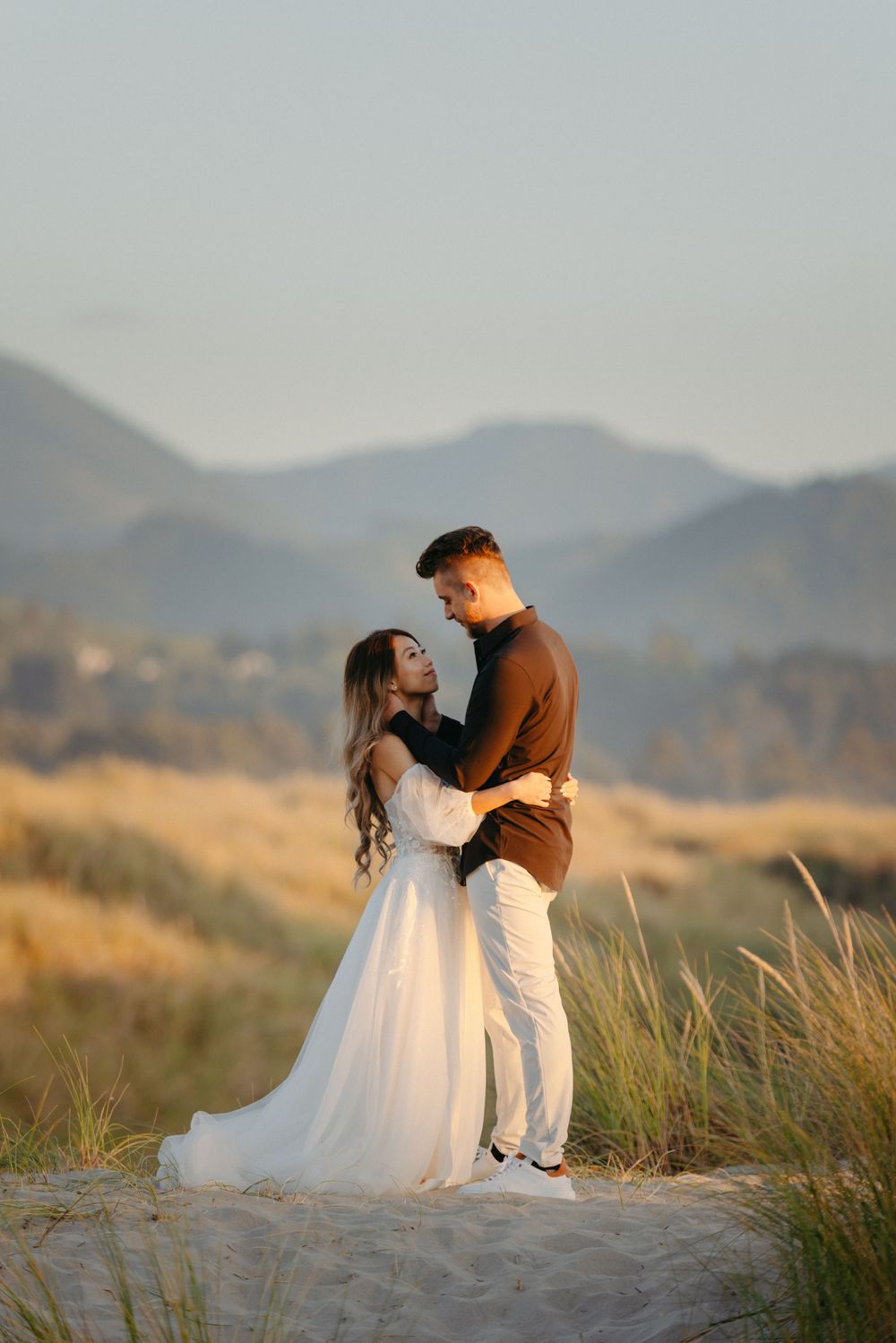 Romantic coastal engagement photo with mountains and golden grass in the background.