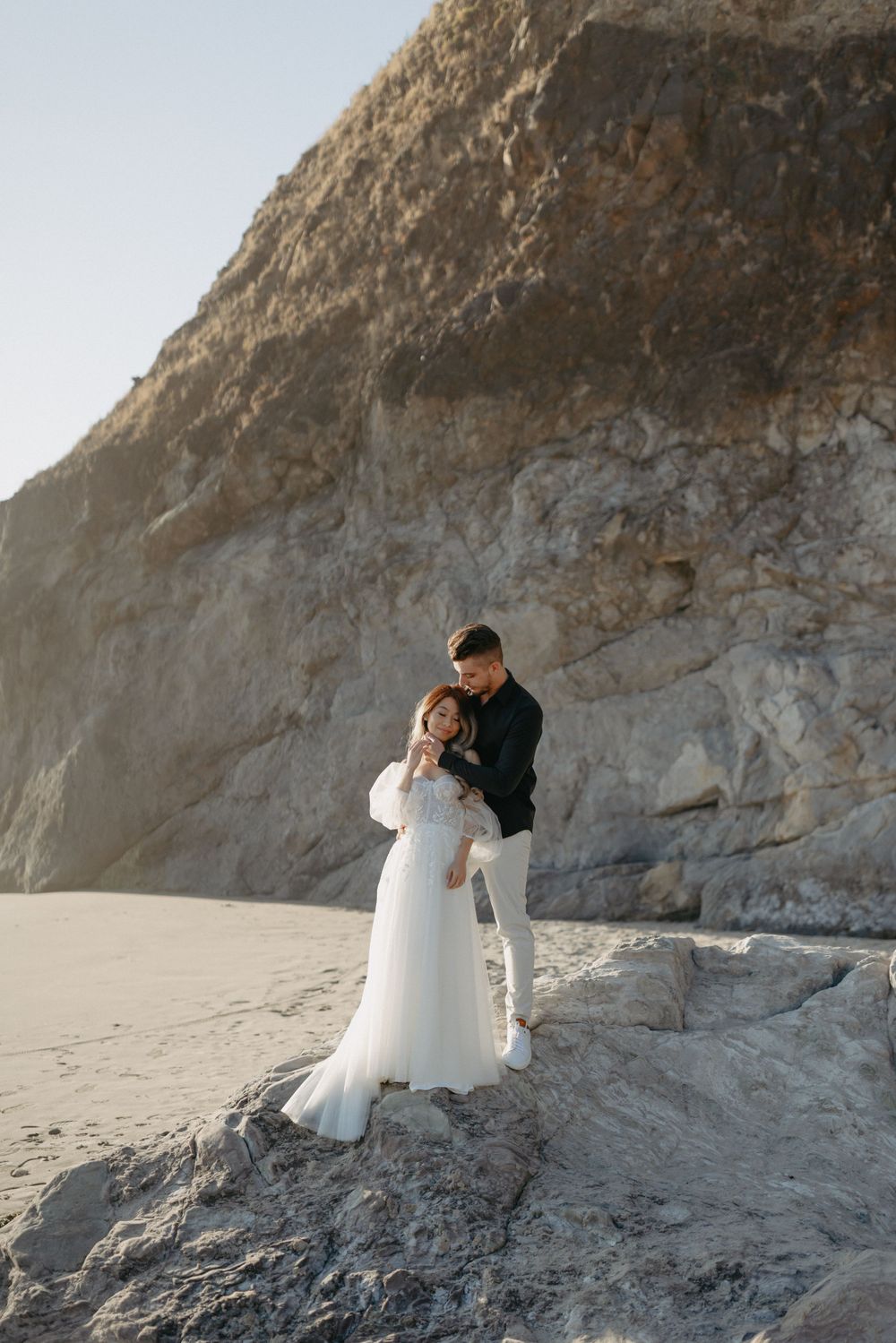 Romantic wedding couple embracing on coastal cliffs overlooking the ocean.