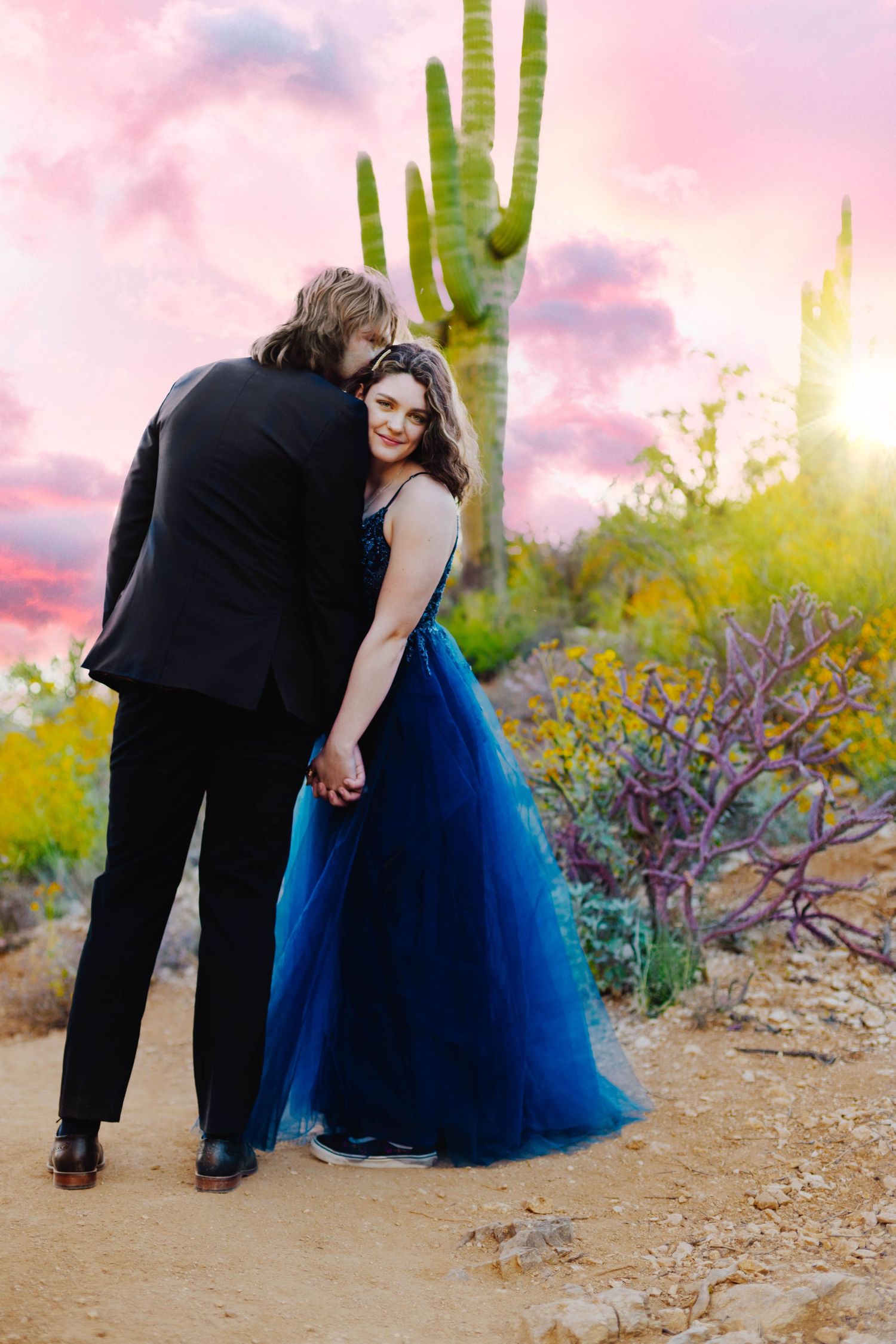 A romantic embrace at sunset with saguaro cactus and pink sky in the background.