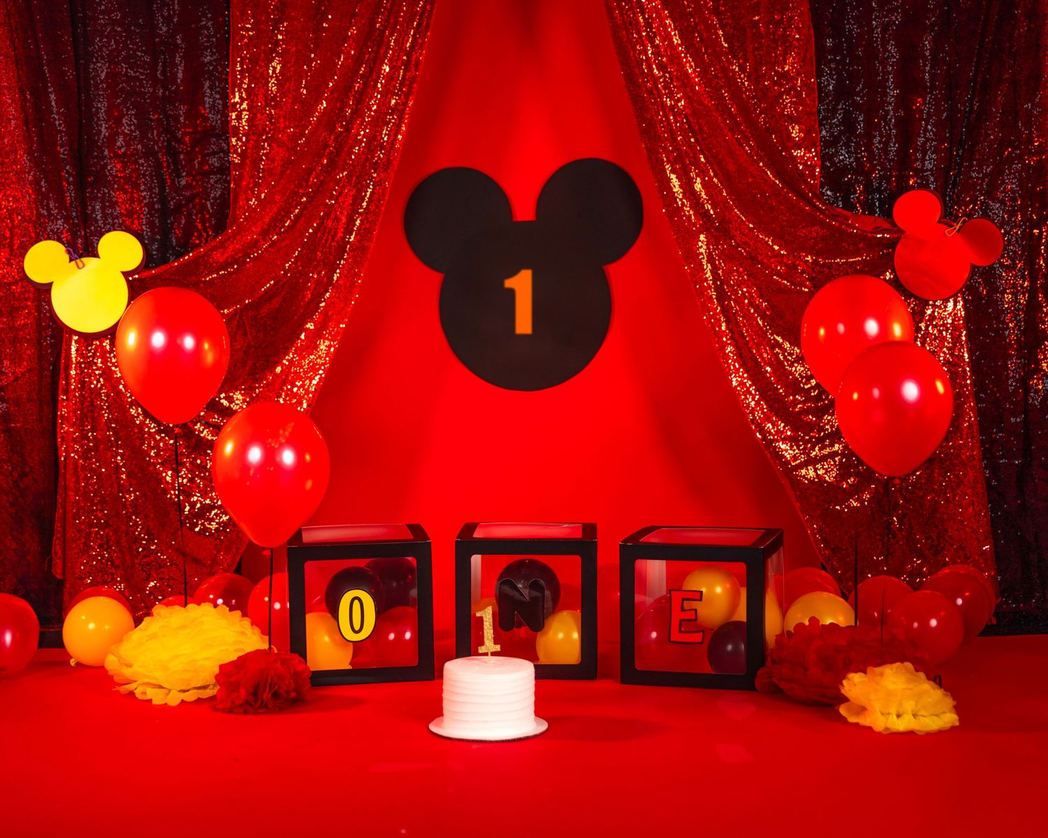 Mickey Mouse themed first birthday party setup with red curtains and balloons against red backdrop.
