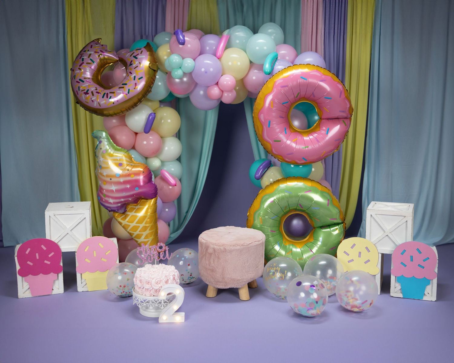 Whimsical party backdrop with giant donut decorations, ice cream cone props, and pastel colored blocks.