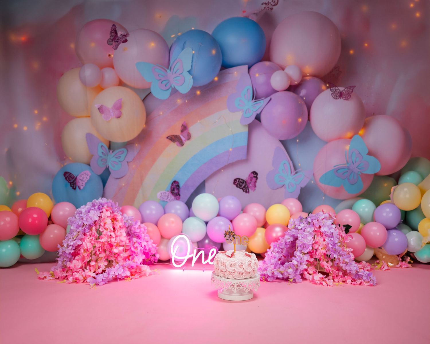 Whimsical balloon backdrop featuring pastel colors, butterflies, and pink floral arrangements on a pink floor.