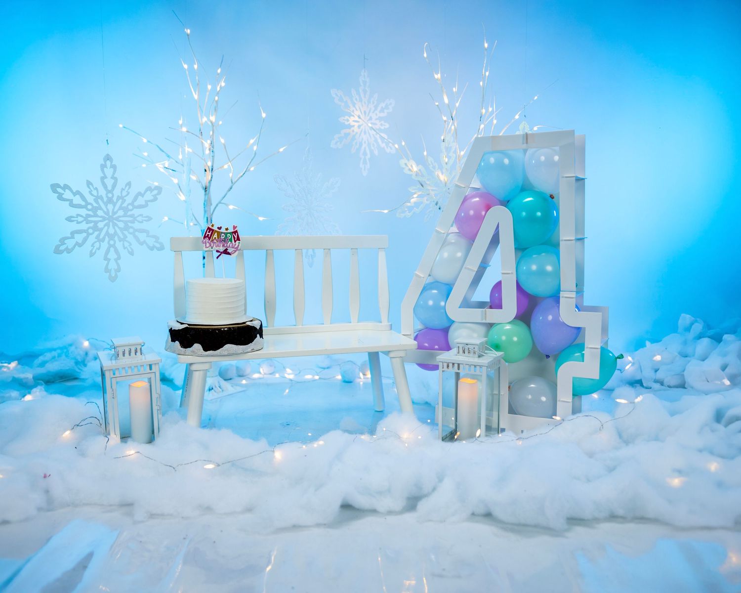 Winter wonderland themed party setup with a number 4, snowflakes, and white bench against blue backdrop.