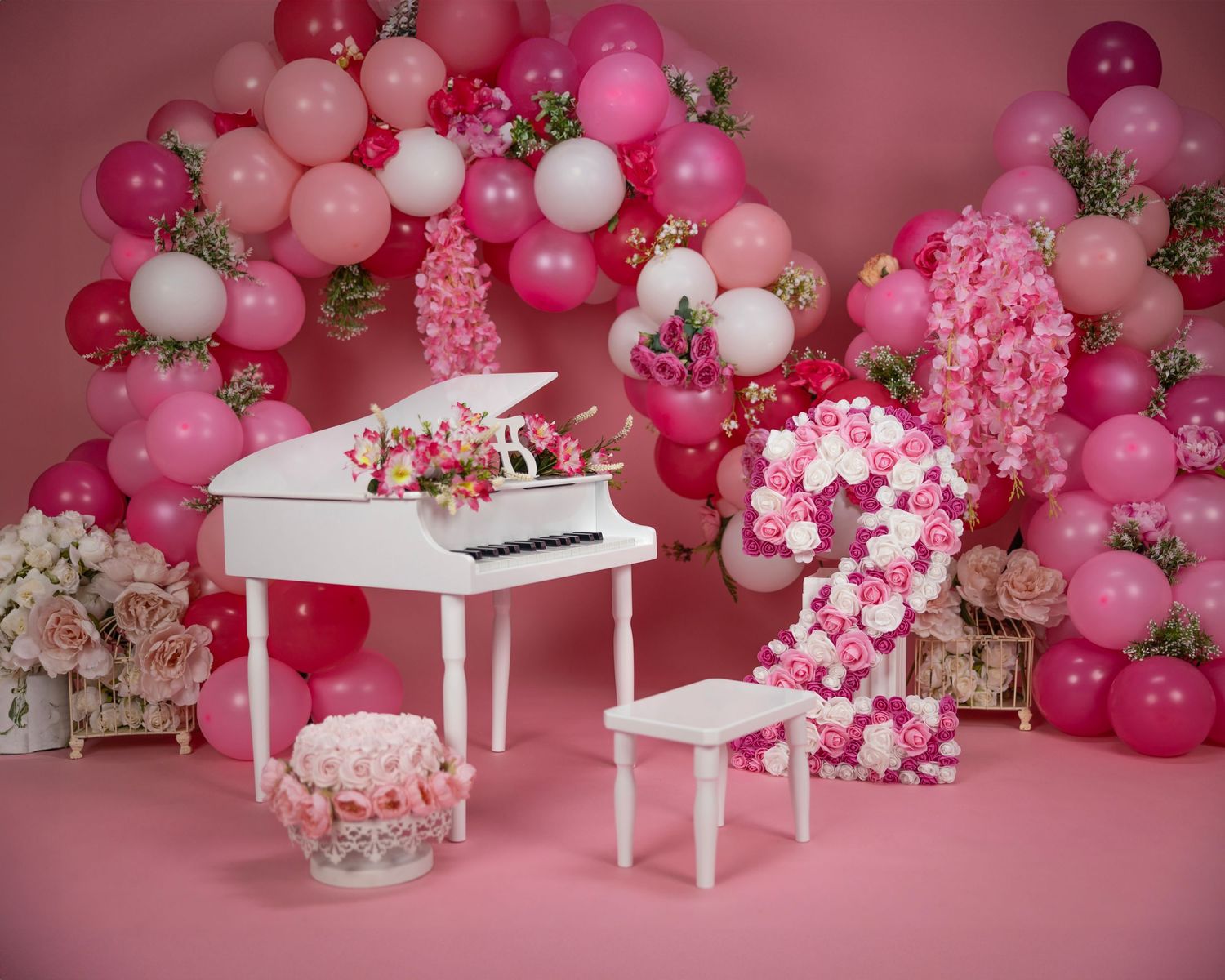 Pink balloon arch with white piano, floral decorations, and piano bench in a romantic setting.
