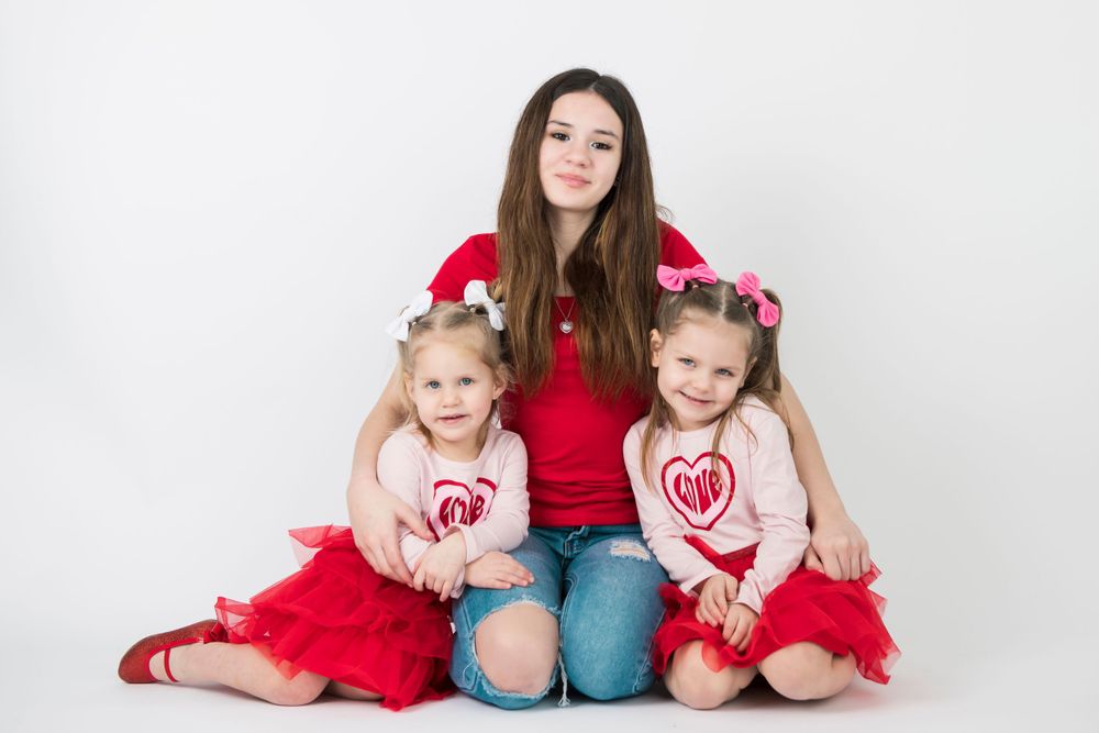 Three people in coordinating red and white outfits sitting together against white backdrop.