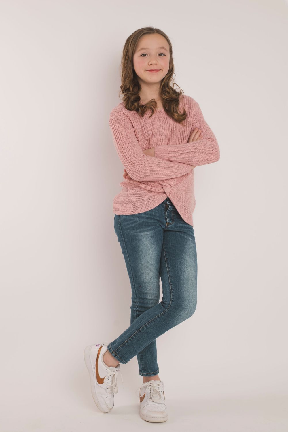 Casual portrait wearing pink sweater and jeans against light background.
