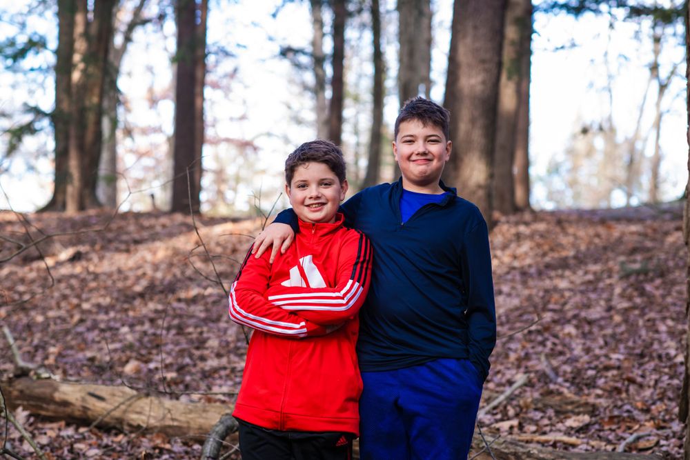 Two people in athletic wear posing among fall leaves in forest setting.
