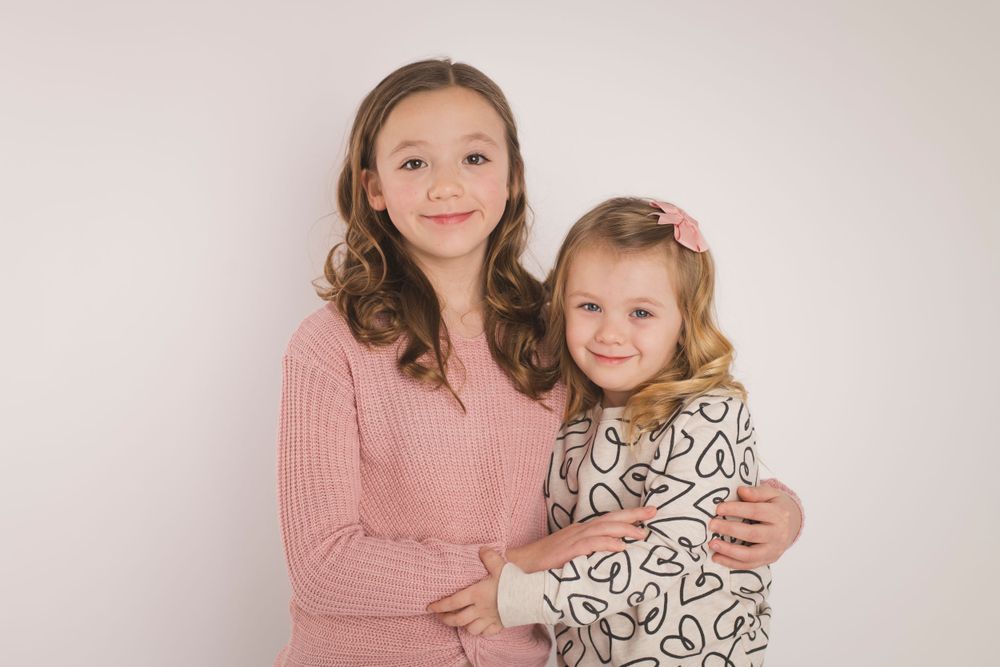 Two people in pink and patterned outfits posing together against white background.