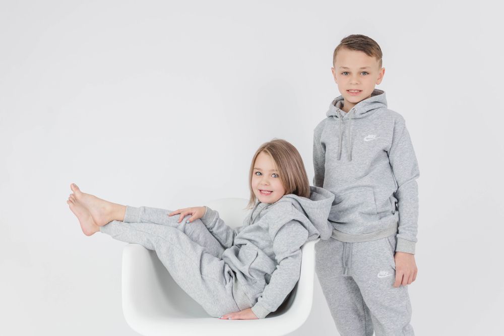 Two children in matching grey sweatsuits posing playfully with chair.