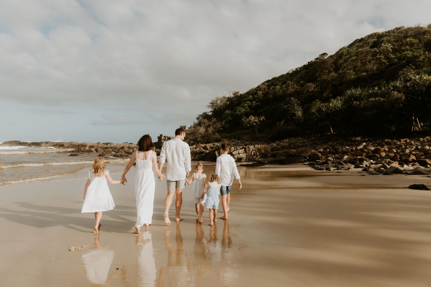 family of 6 walking along the beach at low tide with a green hill in the background