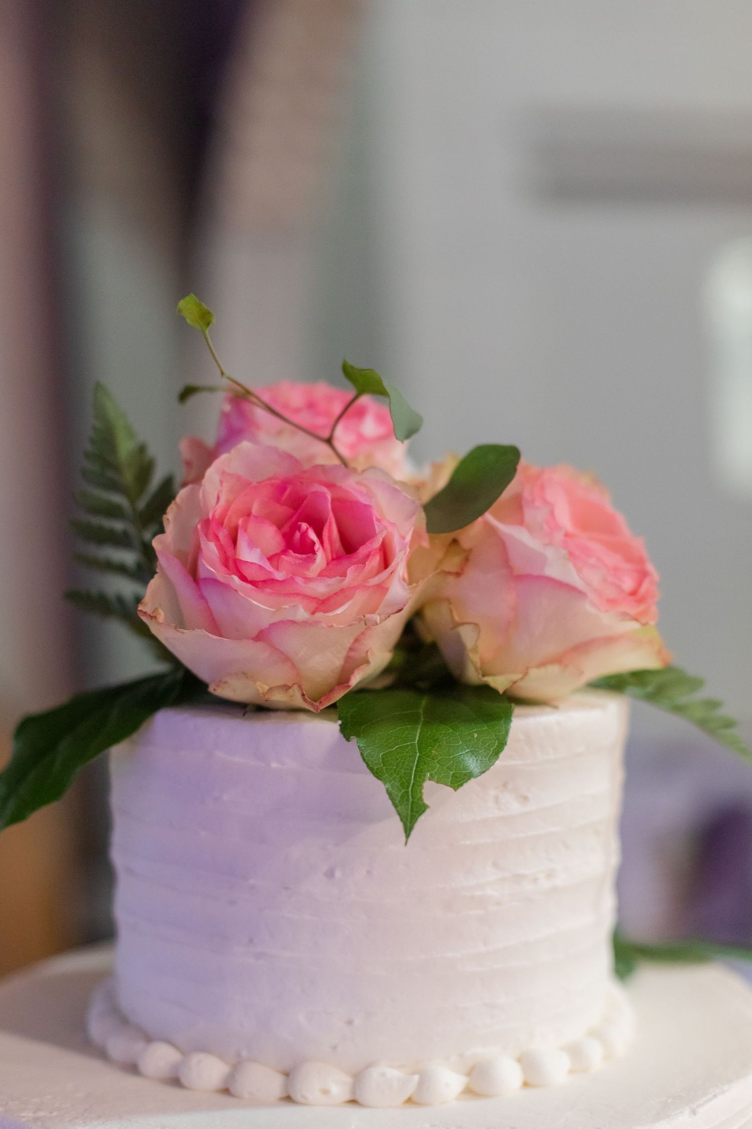 White wedding cake decorated with fresh pink roses and green leaves on top.